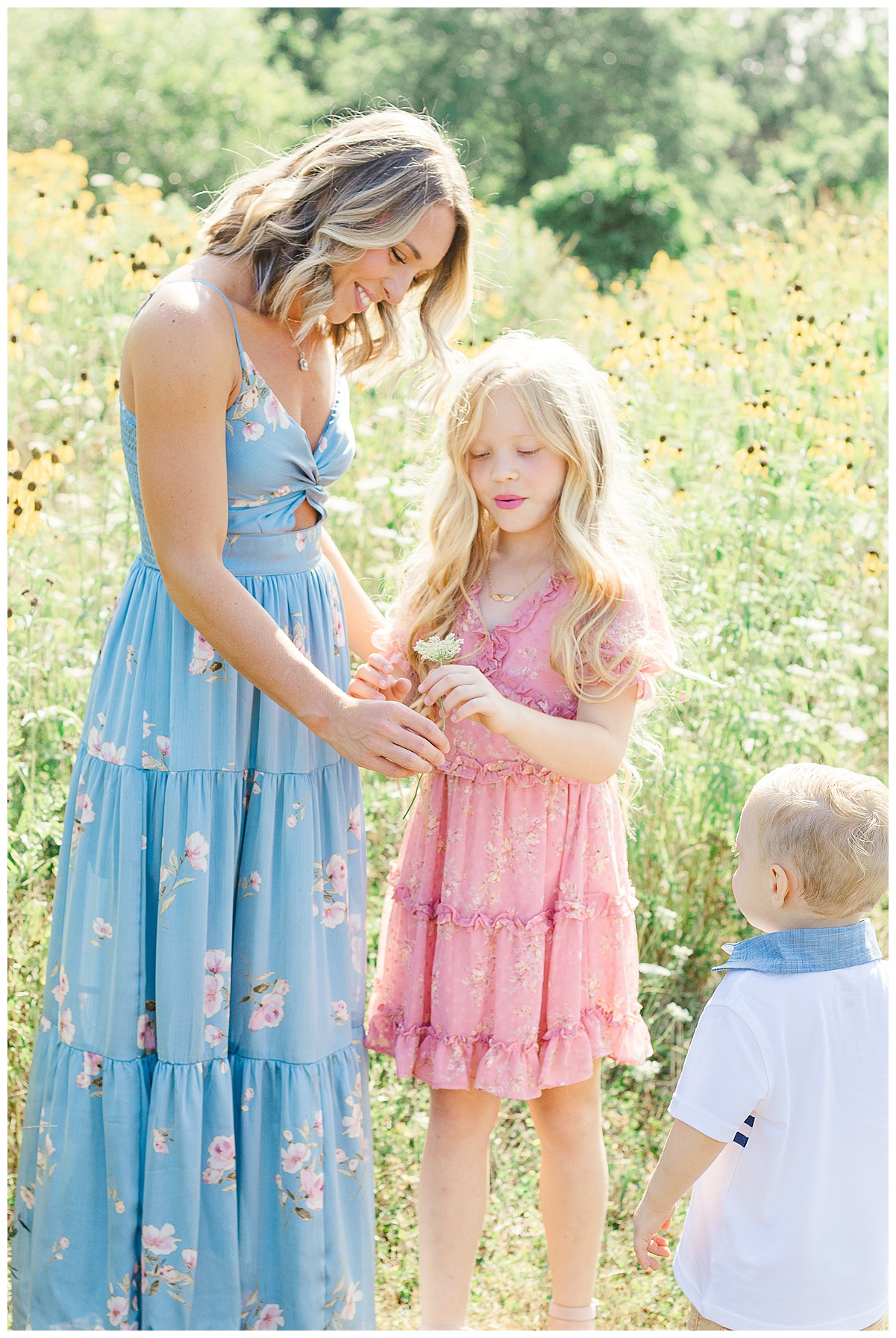 Mom with her 2 kids in front of wildflowers during a family photo session in Pittsburgh, PA. The kids are giving mom flowers.