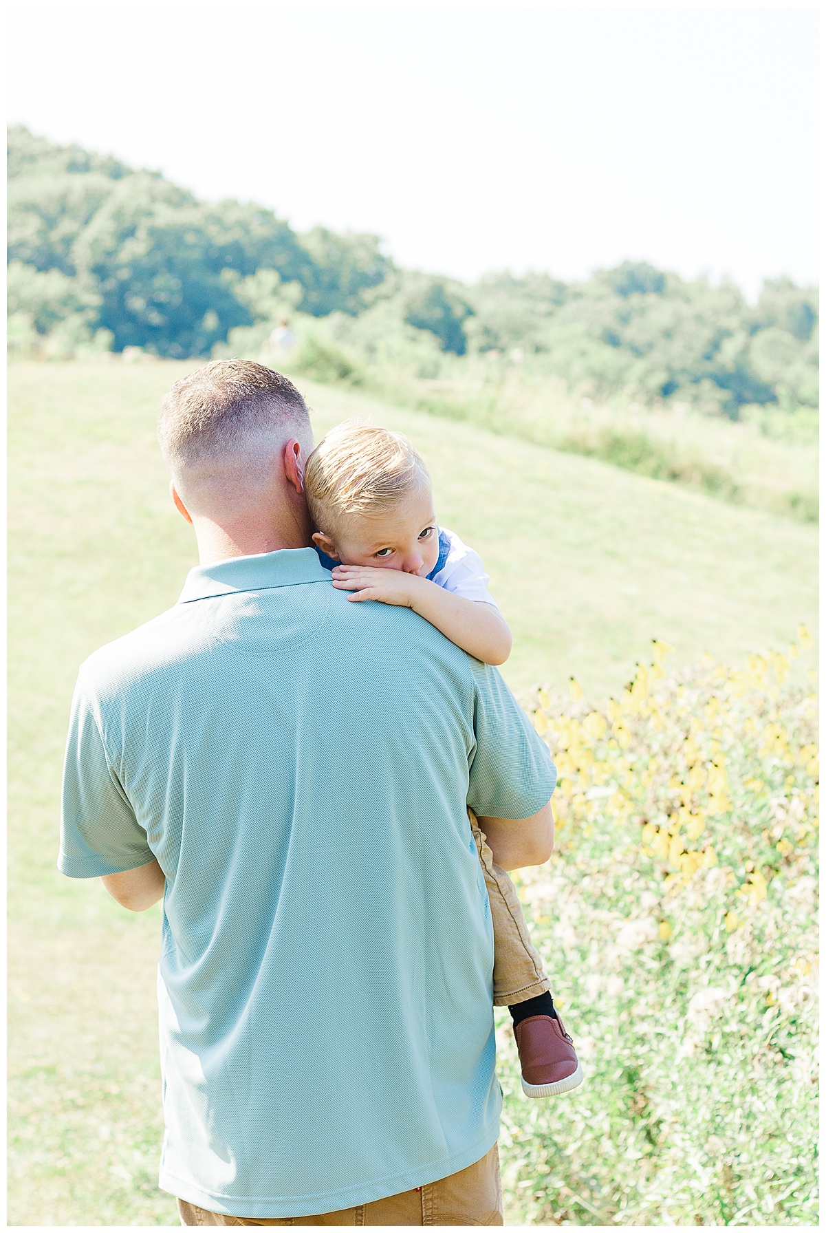 Dad is holding his son during a family outdoor photo session in Pittsburgh, PA. The view is pretty wildflowers.