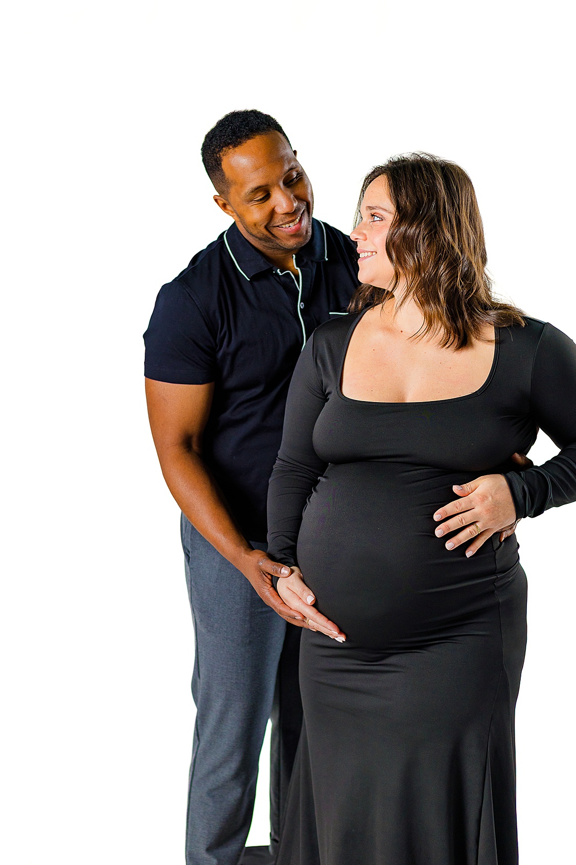 Mom and dad are looking at each other while holding her belly. Taken during an indoor studio maternity session in Pittsburgh, PA