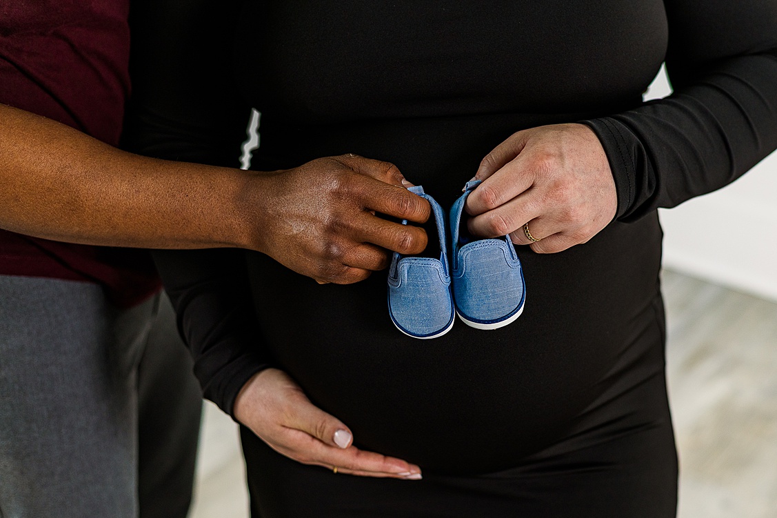 Mom and Dad to be are holding little baby boy shoes during a studio maternity session in Pittsburgh, PA