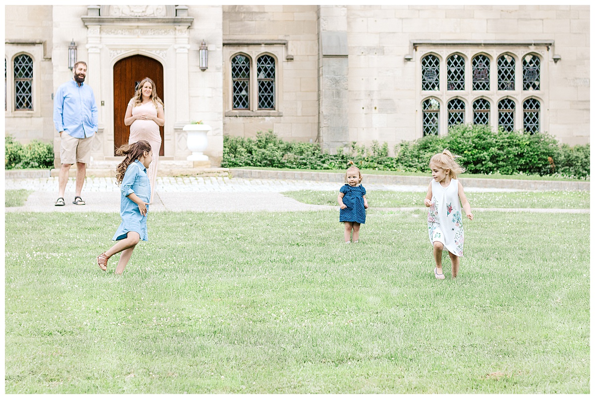 Mom and dad are standing and watching their 3 girls running around during a maternity session in Pittsburgh, PA