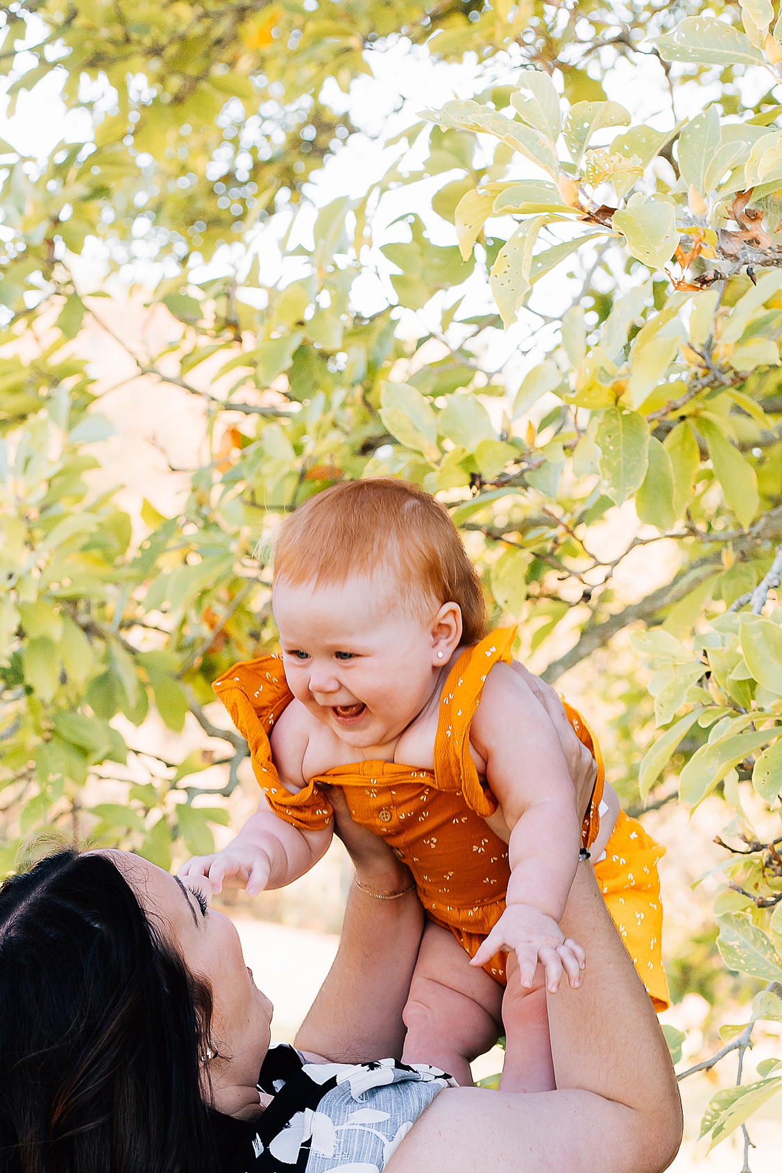Mom holding her daughter up in the air while that baby girl laughs.  Taken during an outdoor fall mini session in pittsburgh, pa.