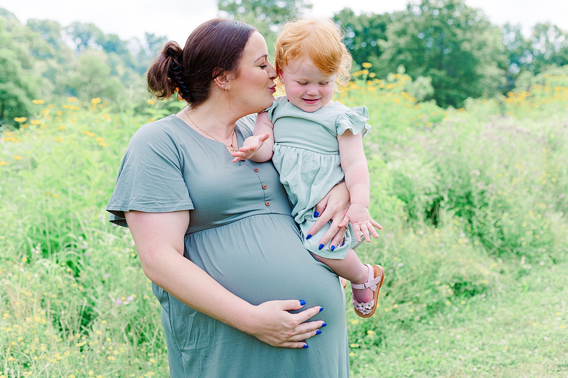 Mom holding her baby bump while kissing her older daughter. Taken by a Pittsburgh baby and pregnancy photographer