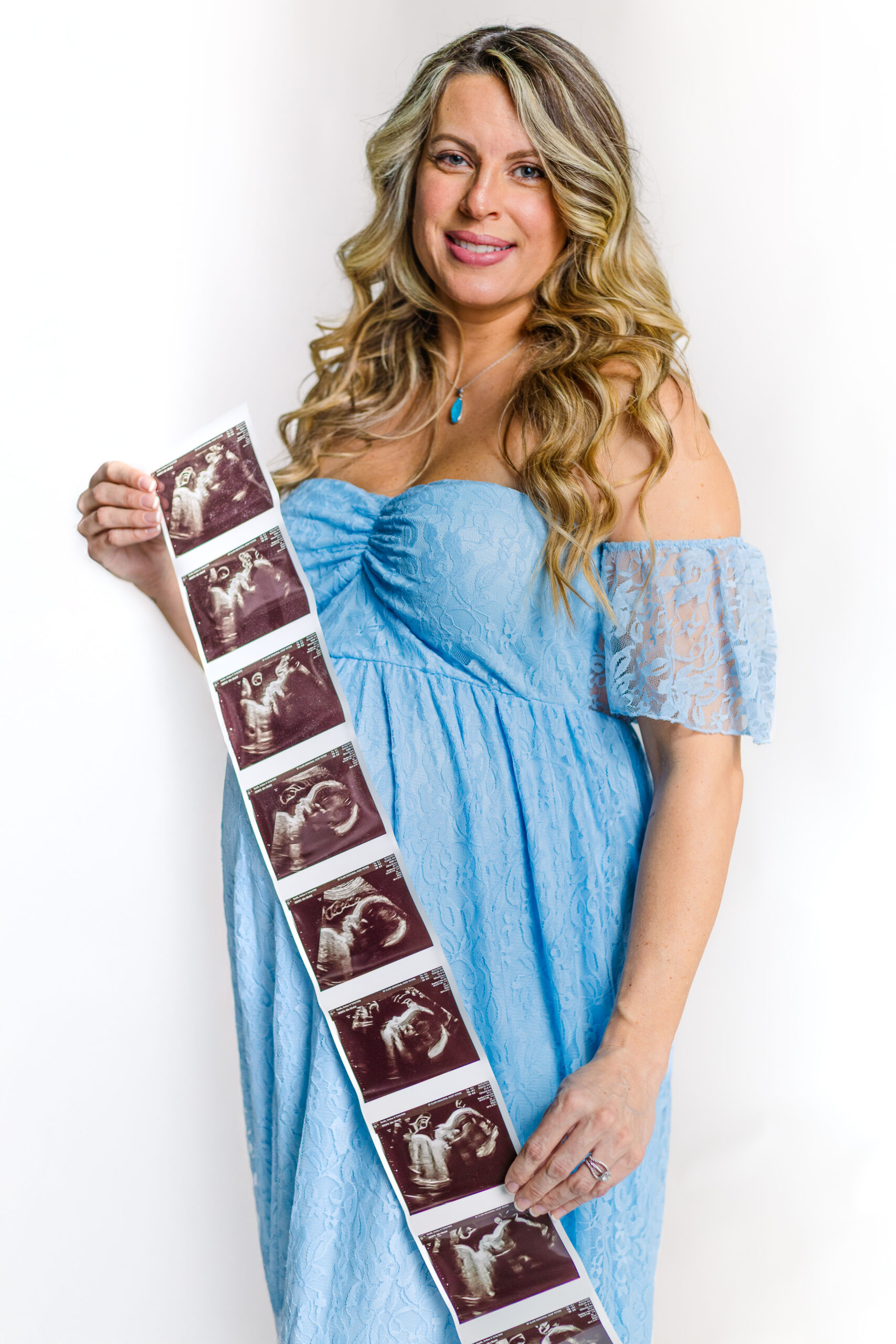 Maternity portrait of a pregnant mother in a soft, blue gown in front of a white studio backdrop