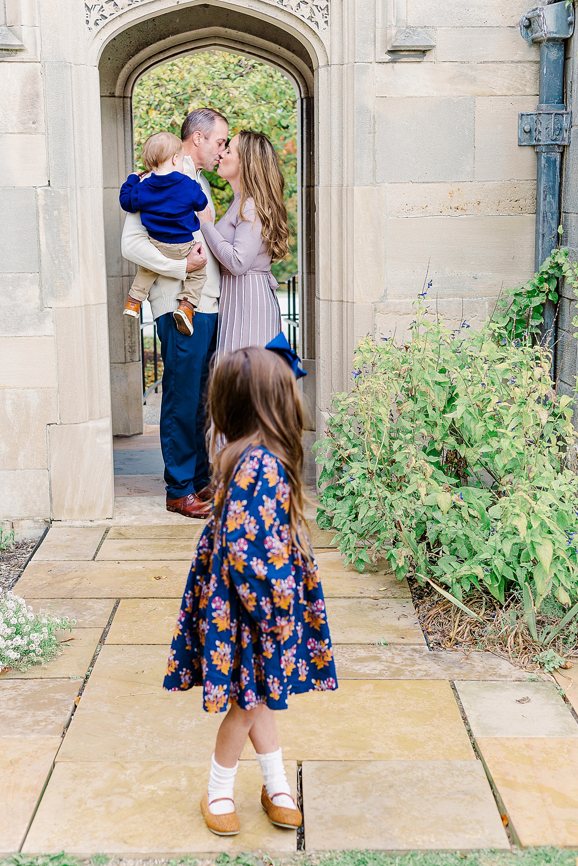 Mom and dad sharing a kiss while the daughter and son look to see what they are doing during an outdoor photo session in Pittsburgh.