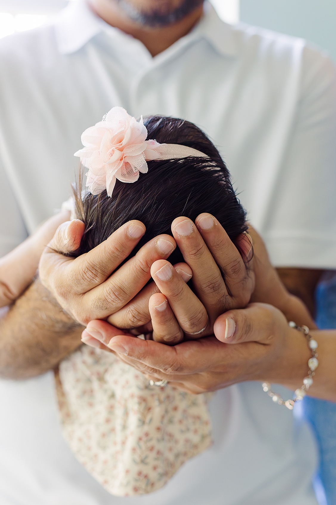 Dad is holding baby girl in his arms while mom's hands are below dads.  This sweet moment is captured by a an in-home newborn photography Pittsburgh.