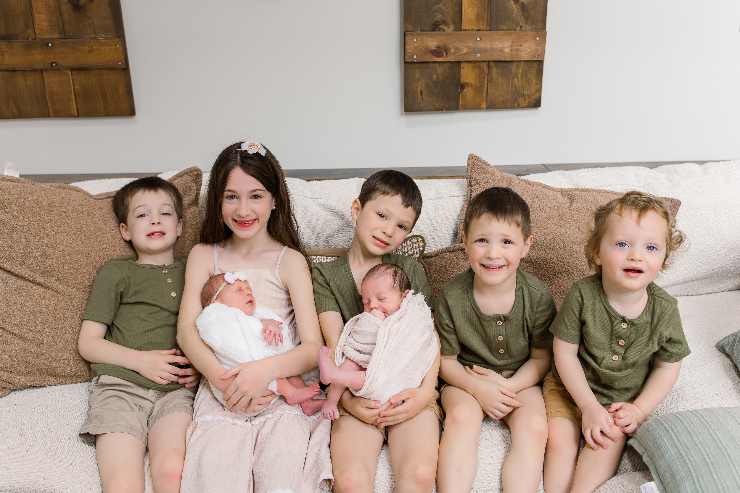 All seven siblings are sitting together. The two oldest are holding the newest newborn twins. Taken during a newborn Pittsburgh session in their house.