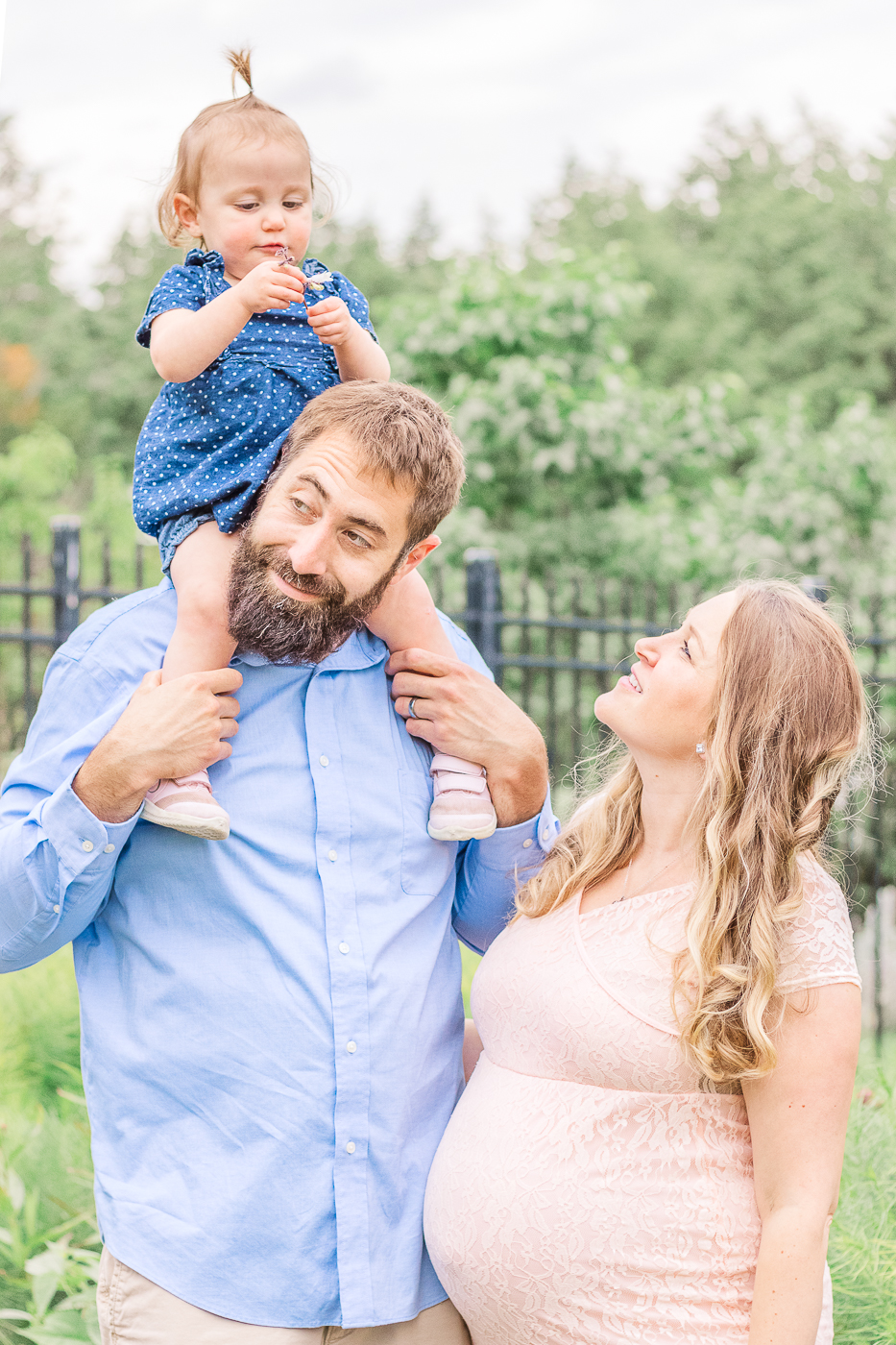 Dad holding toddler on his shoulder while mom looks on lovingly and little girl admires a flower during a Wexford maternity photoshoot