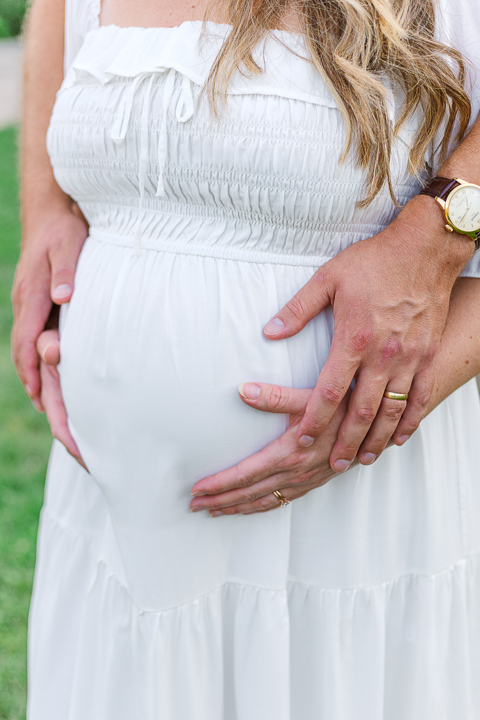 Mom and Dad holding moms baby bump. Mom is wearing a beautiful white dress. Taken during a maternity photoshoot in Pittsburgh.