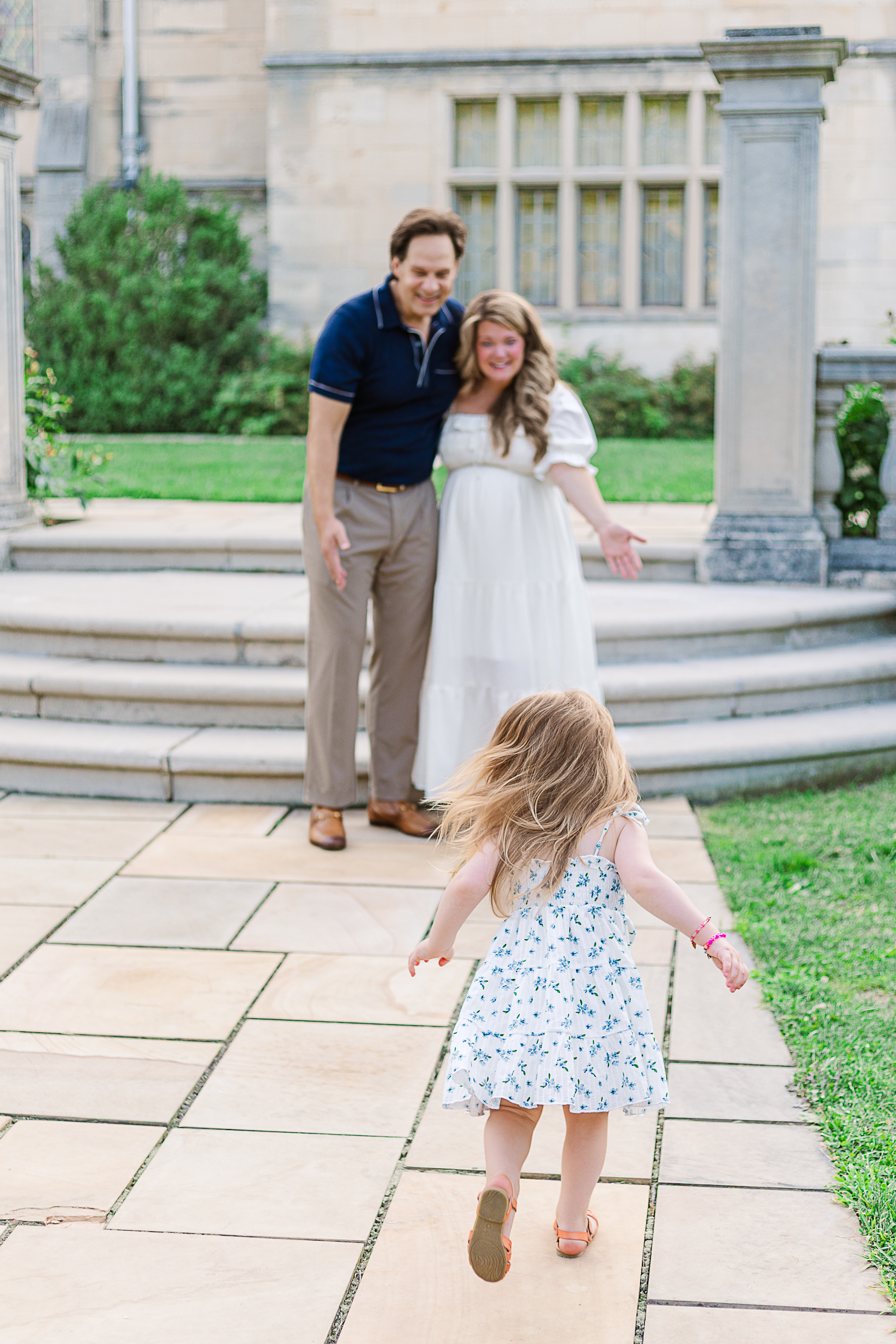 Little girl is running to her mom and dad during their maternity photography session in Pittsburgh at the beautiful Hartwood Acres.